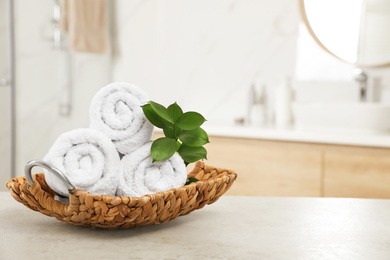 Photo of Rolled fresh towels and green leaves on grey table in bathroom. Space for text