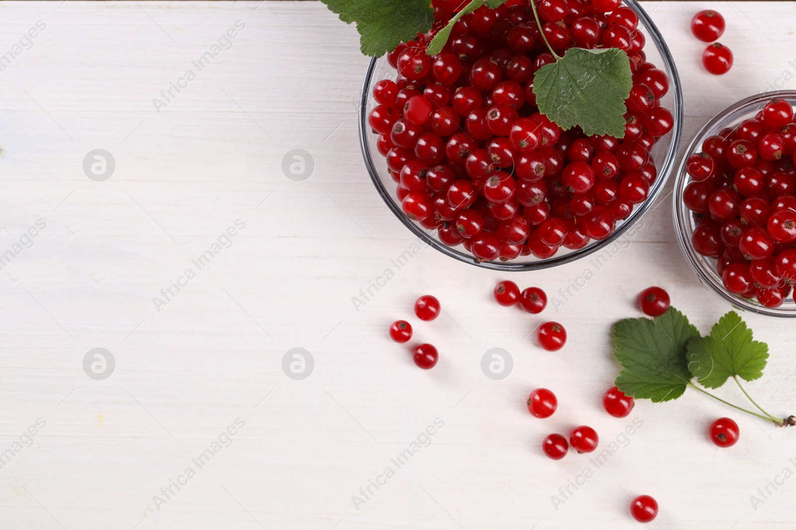 Photo of Many ripe red currants and leaves on white wooden table, flat lay. Space for text