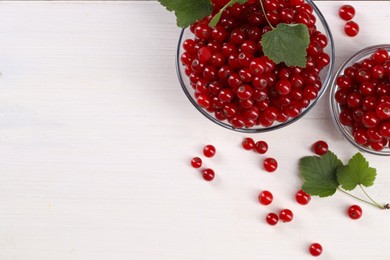 Many ripe red currants and leaves on white wooden table, flat lay. Space for text