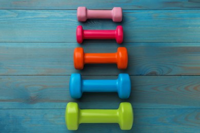 Different dumbbells on light blue wooden table, flat lay