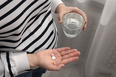 Pregnant woman with glass of water and pill at home, closeup