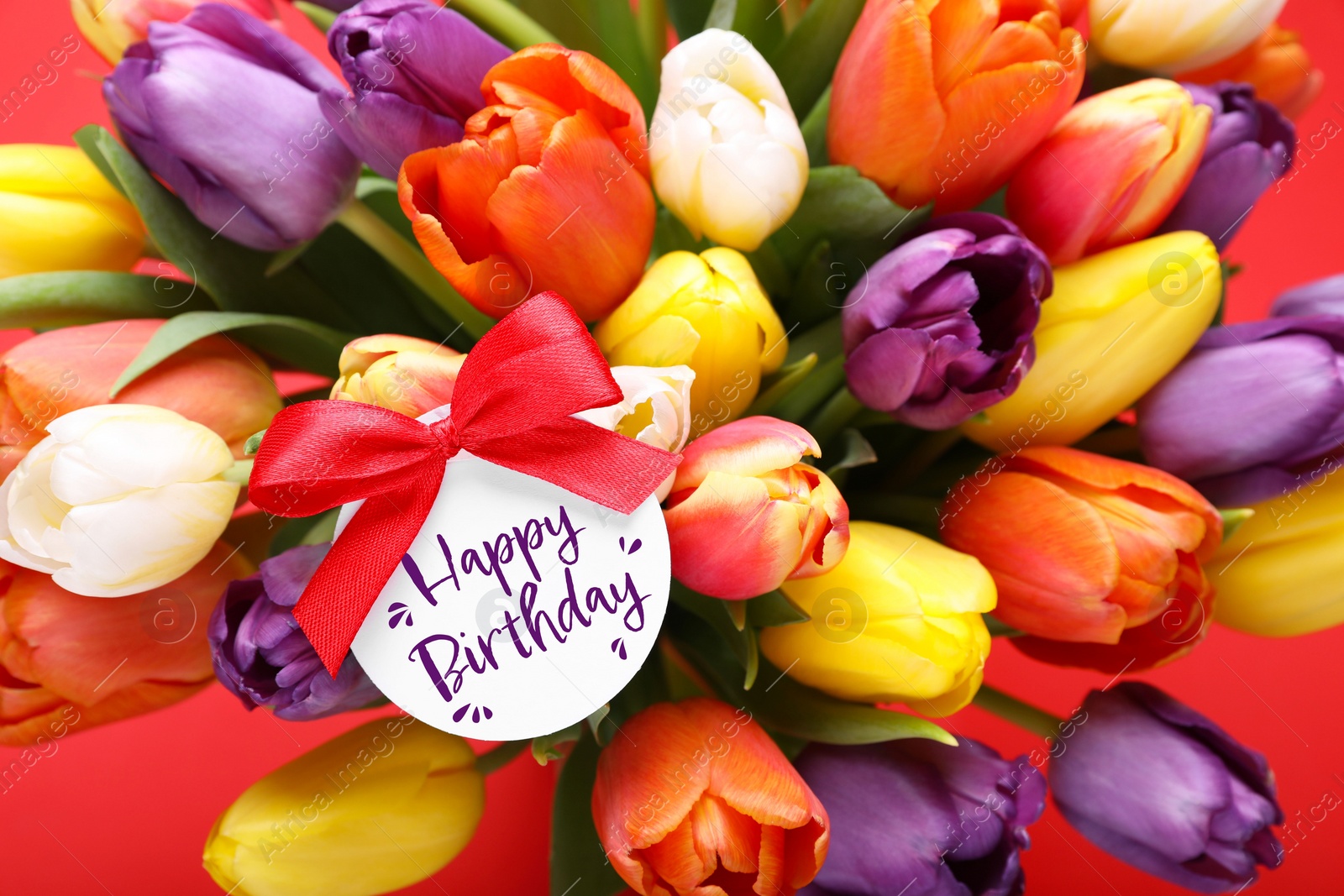 Image of Beautiful bouquet of tulip flowers with Happy Birthday card on orange background, closeup