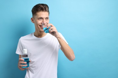 Young man using mouthwash on light blue background, space for text