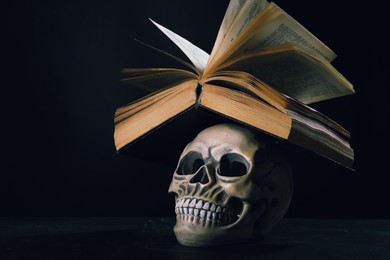 Human skull and old book on black table. Space for text