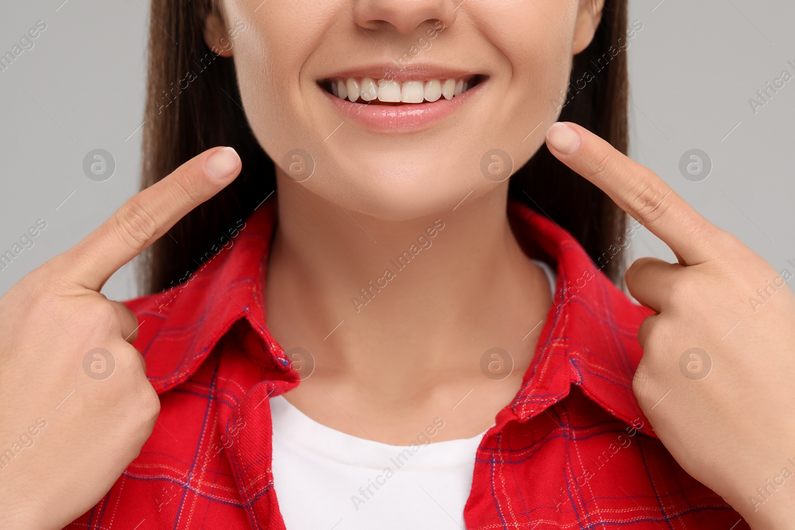 Photo of Woman pointing at her clean teeth and smiling on light grey background, closeup