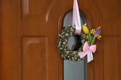 Photo of Wreath made of beautiful willow branches, pink bow and colorful tulip flowers on wooden door, space for text