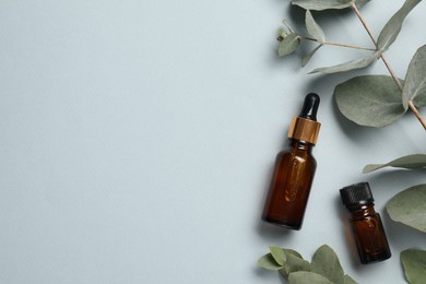 Aromatherapy. Bottles of essential oil and eucalyptus leaves on light grey background, flat lay. Space for text