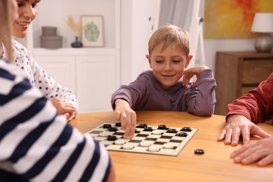 Photo of Family playing checkers at wooden table in room