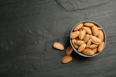 Photo of Ceramic bowl with almonds on black table, flat lay and space for text. Cooking utensil
