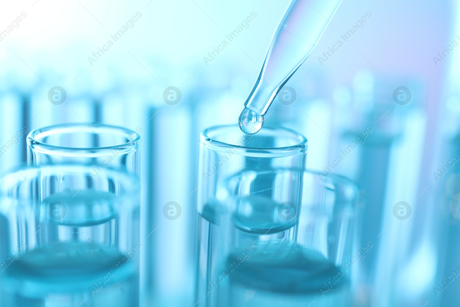 Photo of Dripping liquid from pipette into test tube on light blue background, closeup