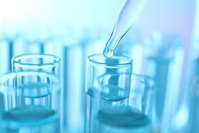 Photo of Dripping liquid from pipette into test tube on light blue background, closeup