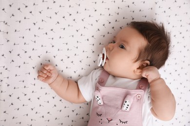 Photo of Cute little baby with pacifier lying on blanket, top view. Bedtime