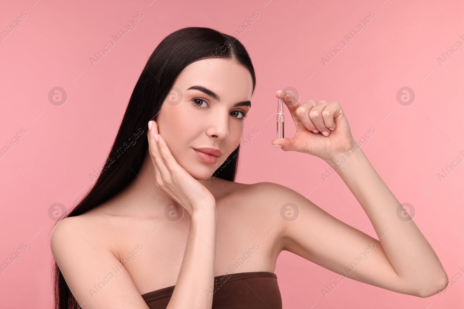 Photo of Beautiful young woman holding skincare ampoule on pink background