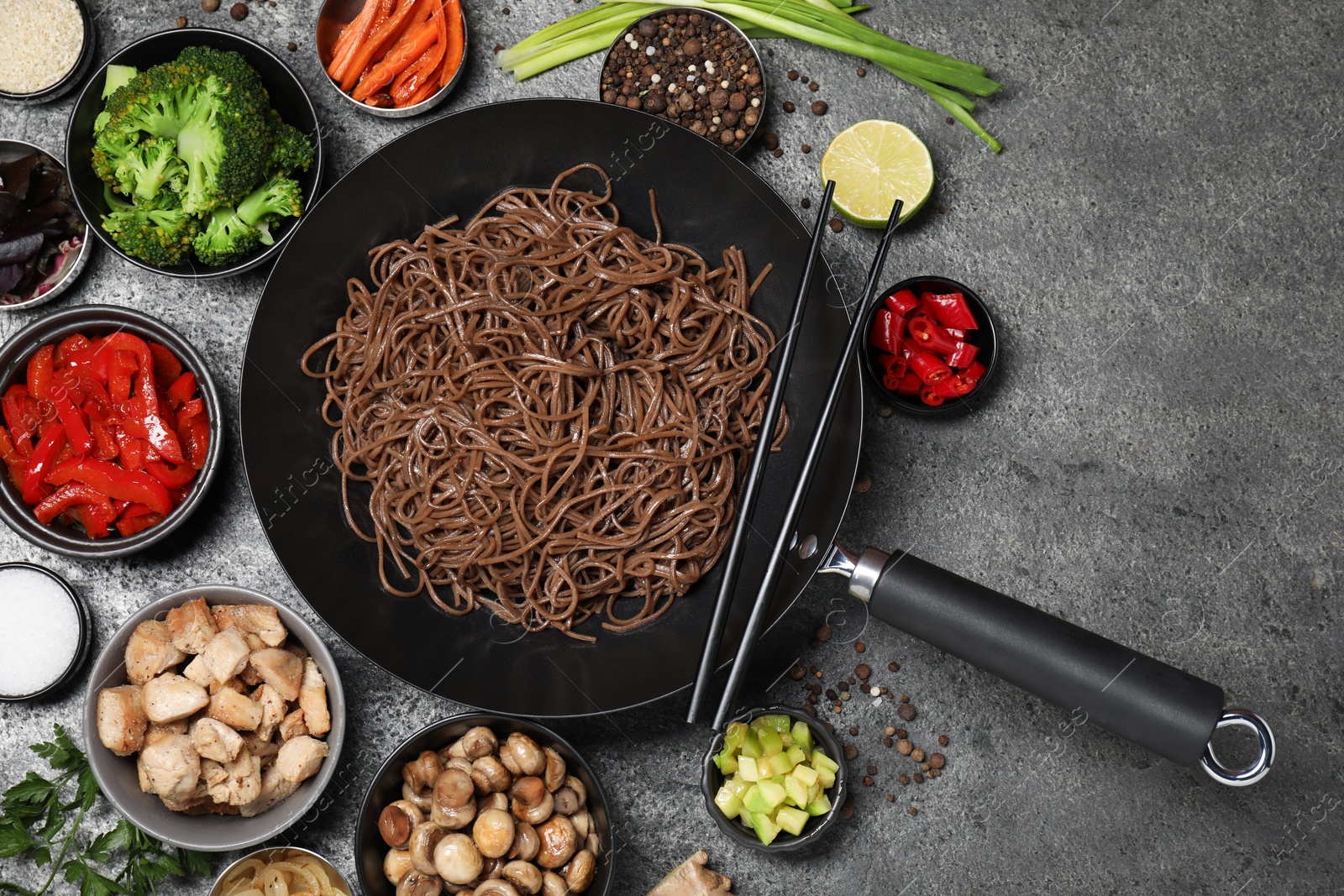 Photo of Wok with noodles, chicken and other products on grey table, flat lay