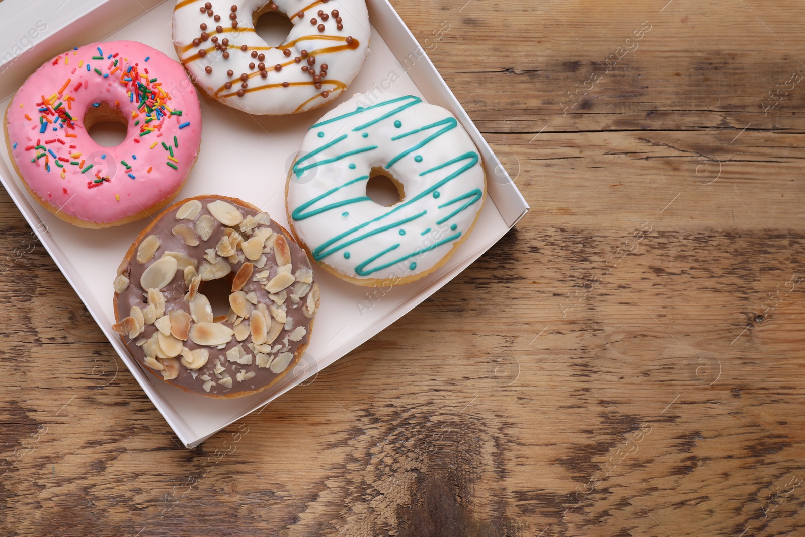 Photo of Box with different tasty glazed donuts on wooden table, top view. Space for text
