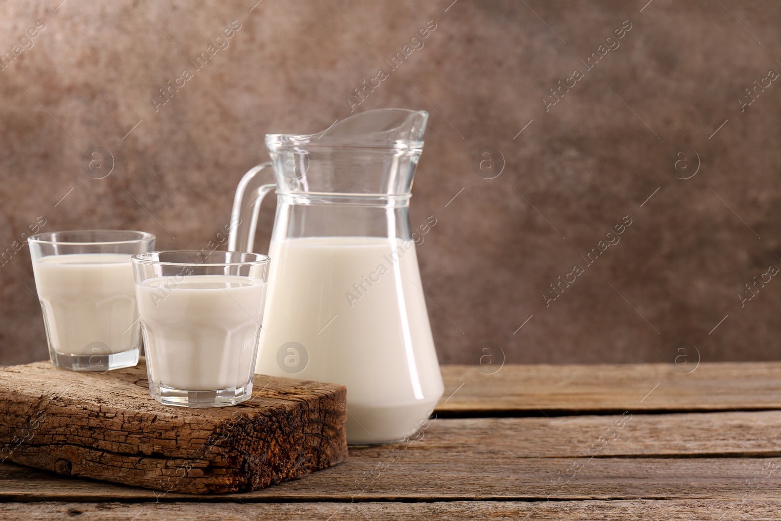 Photo of Jug and glasses of fresh milk on wooden table, space for text