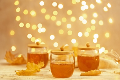 Glass jars with sweet honey on table against blurred lights. Space for text