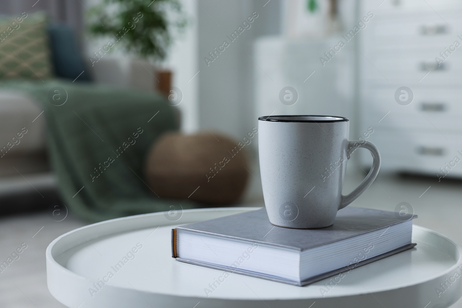 Photo of Ceramic mug and book on white table indoors. Mockup for design