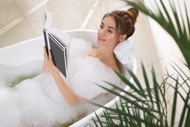 Beautiful woman reading book while enjoying bubble bath at home