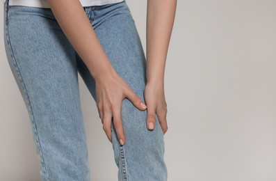 Photo of Woman suffering from pain in her knee on light grey background, closeup with space for text. Arthritis symptoms