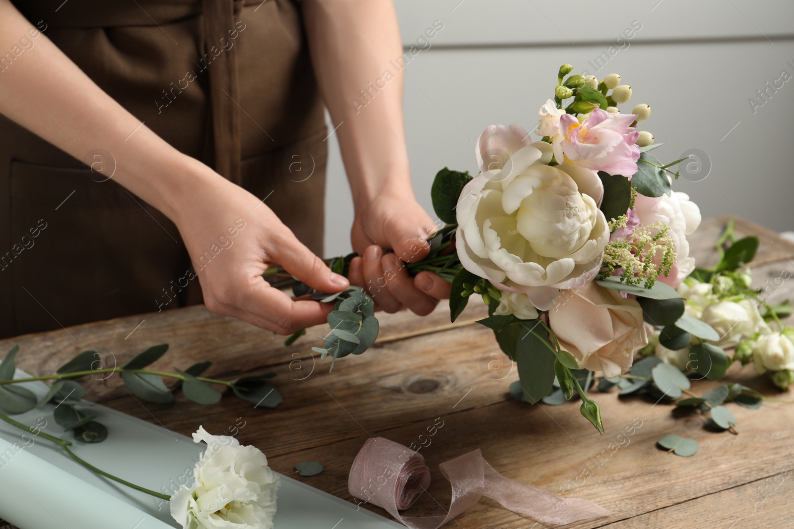 Photo of Florist creating beautiful bouquet at wooden table indoors, closeup