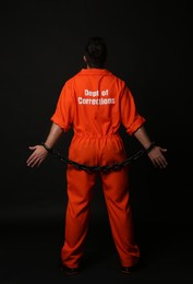 Photo of Prisoner in jumpsuit with chained hands on black background, back view