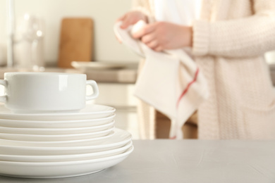 Photo of Woman wiping plate with towel in kitchen, focus on stack of clean dishes
