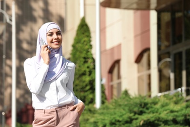 Photo of Muslim woman in hijab talking on phone outdoors