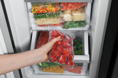 Photo of Woman taking plastic bag with frozen tomatoes from refrigerator, closeup