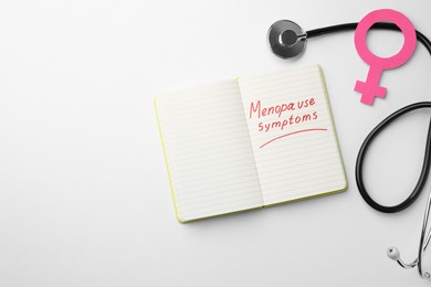 Photo of Notebook with words Menopause Symptoms, stethoscope and female gender sign on white table, flat lay. Space for text