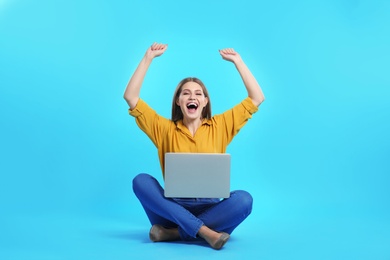 Emotional young woman with laptop celebrating victory on color background