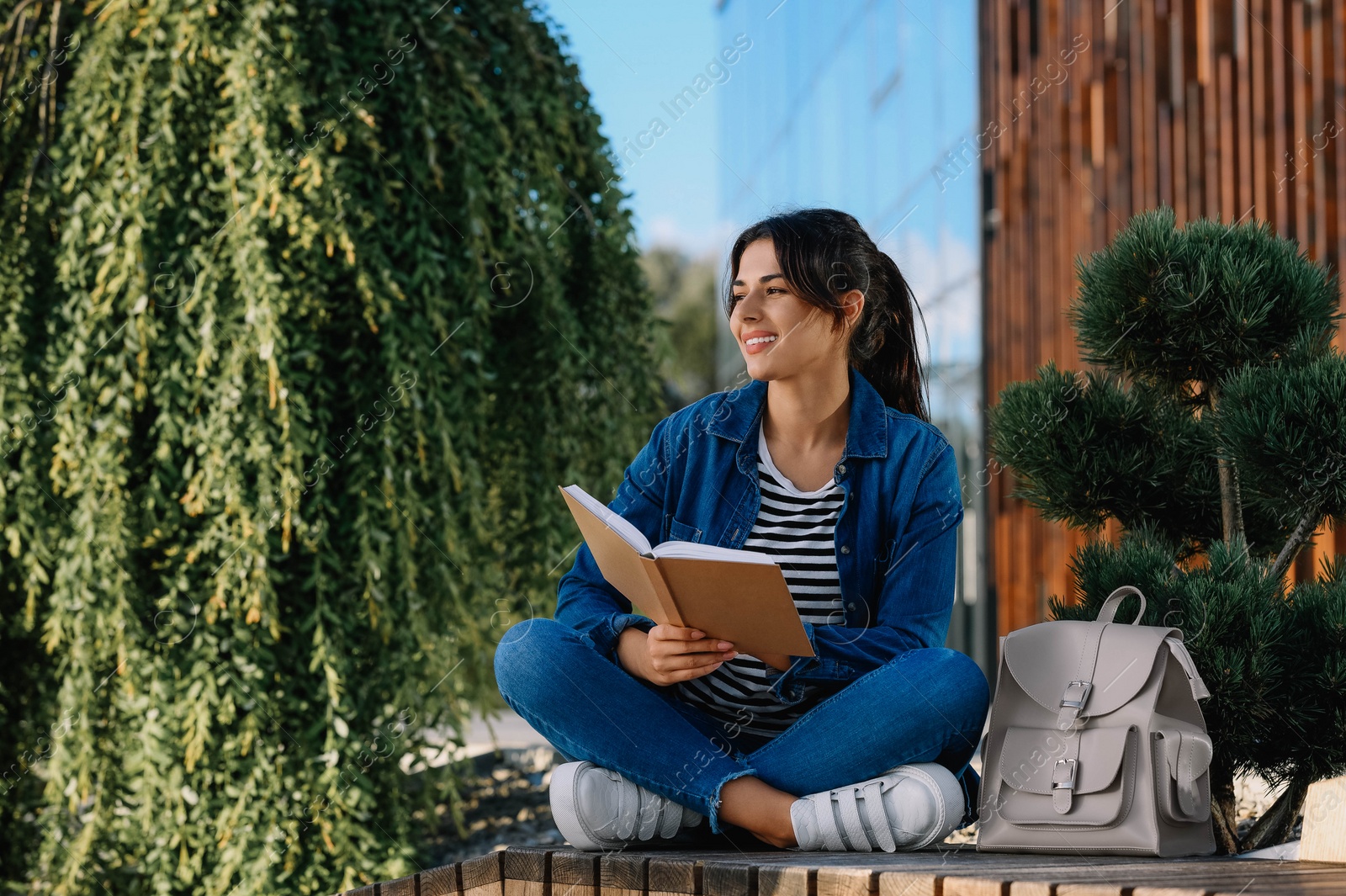 Photo of Young woman reading book on bench outdoors