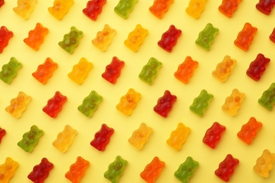 Delicious bright jelly bears on yellow background, flat lay