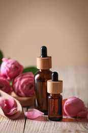 Photo of Bottles of essential oil and roses on white wooden table against beige background
