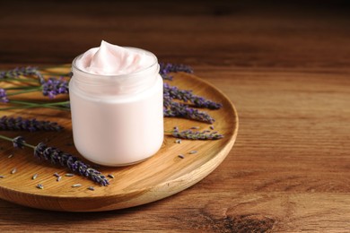 Jar of face cream and lavender flowers on wooden table, space for text