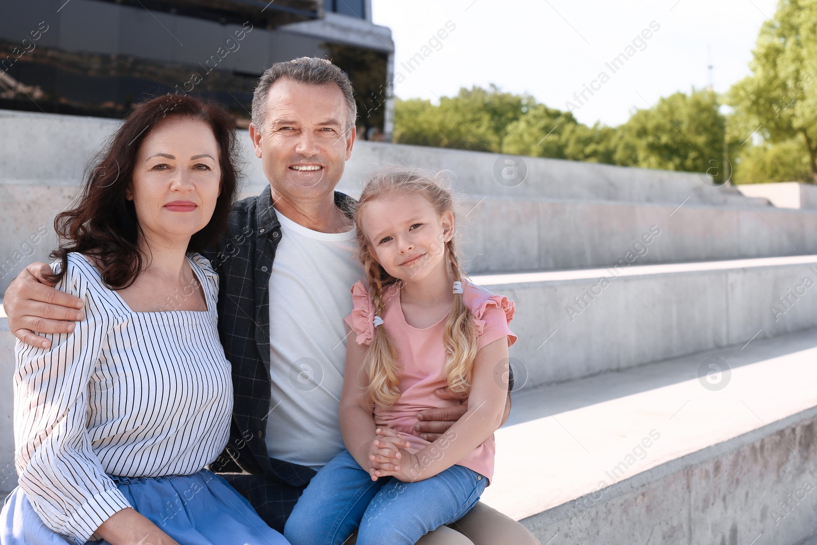 Photo of Couple of pensioners with granddaughter sitting outdoors. Space for text