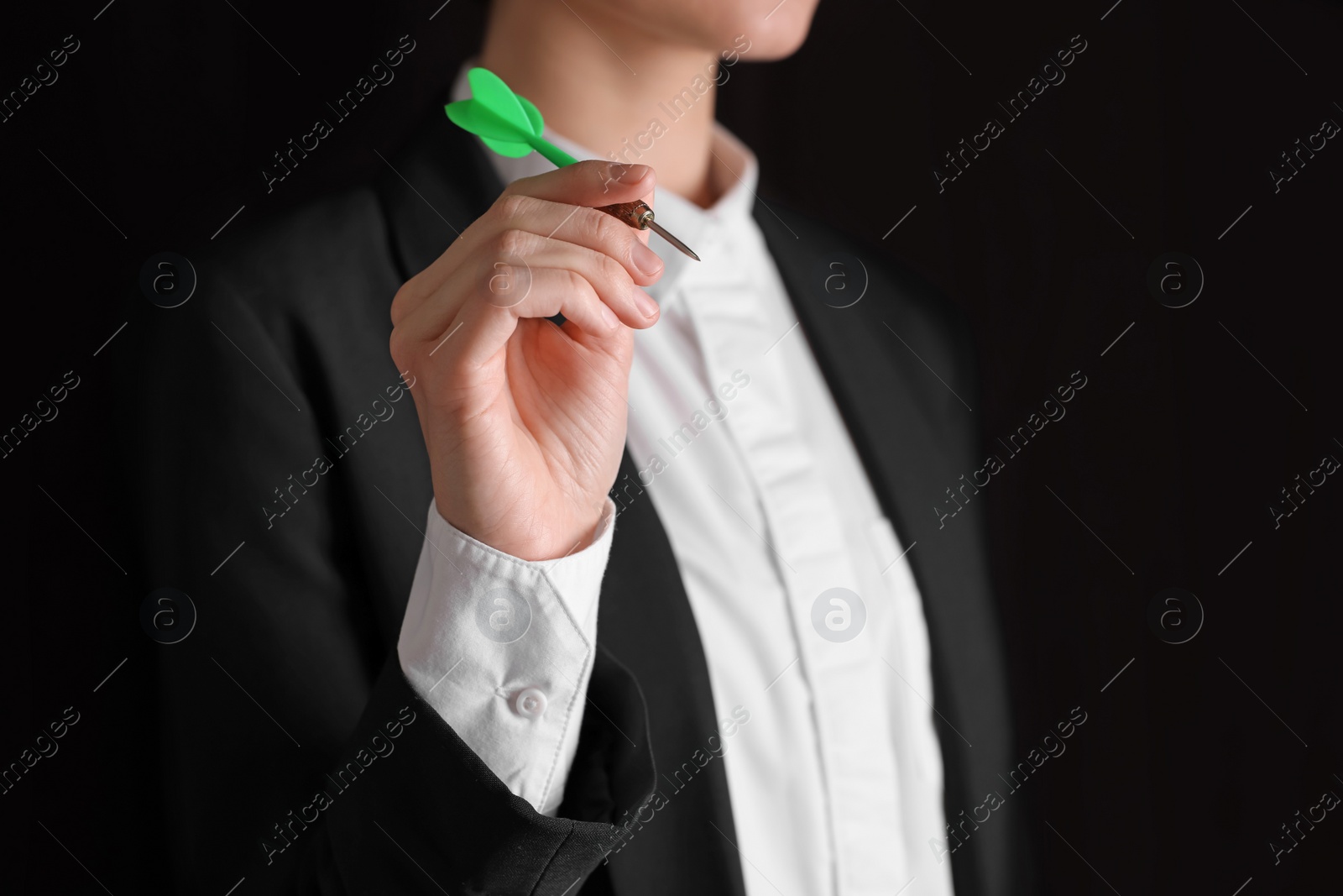 Photo of Businesswoman holding green dart on black background, closeup