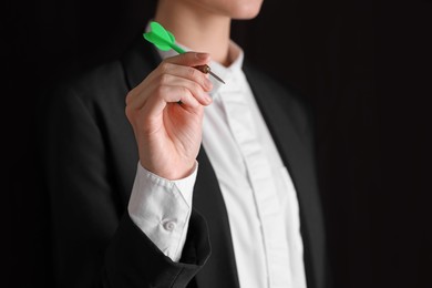 Businesswoman holding green dart on black background, closeup