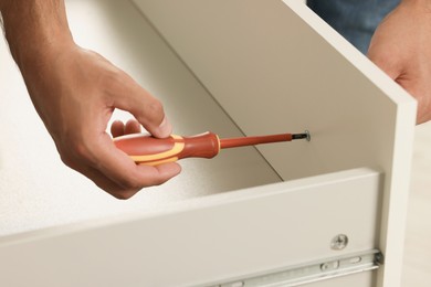 Photo of Man with screwdriver assembling drawer, closeup view