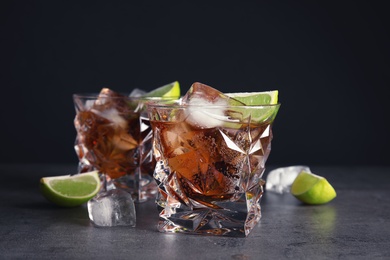 Glass of refreshing drink with ice cubes and lime on table against dark background
