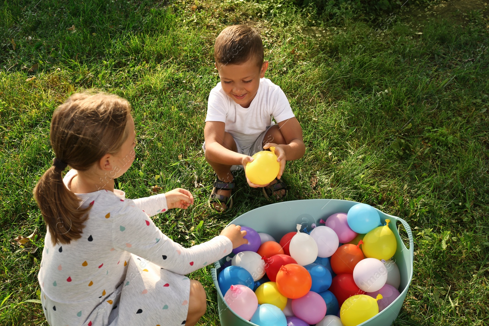 Photo of Little children with basin of water bombs on green grass