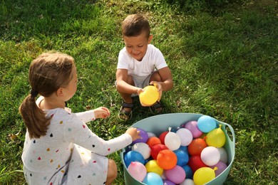 Little children with basin of water bombs on green grass