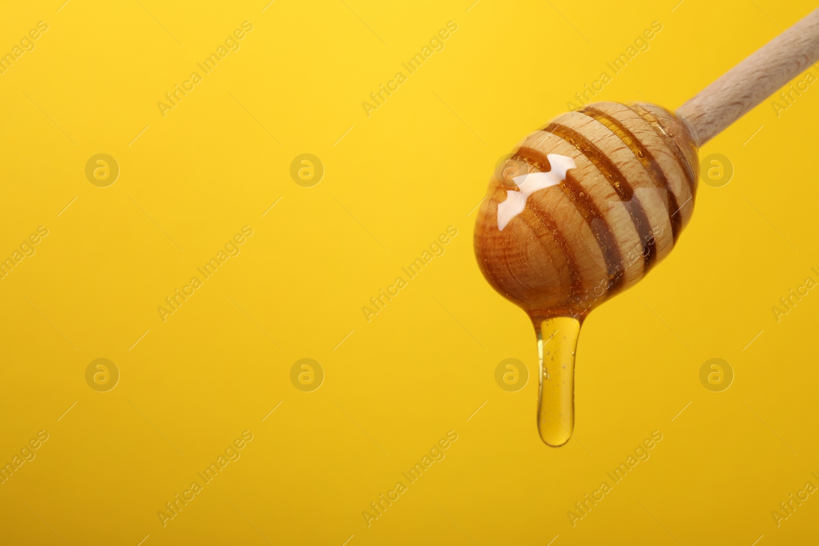 Photo of Pouring honey from dipper against yellow background, closeup. Space for text