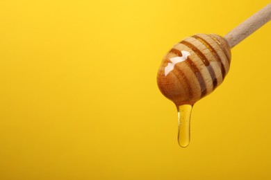 Pouring honey from dipper against yellow background, closeup. Space for text
