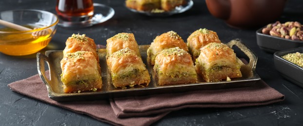 Photo of Delicious fresh baklava with chopped nuts served on grey textured table, closeup. Eastern sweets