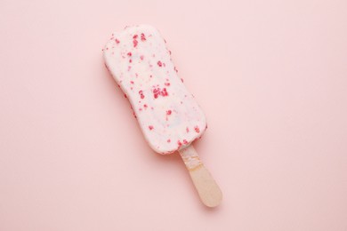 Delicious glazed ice cream bar on pale pink background, top view