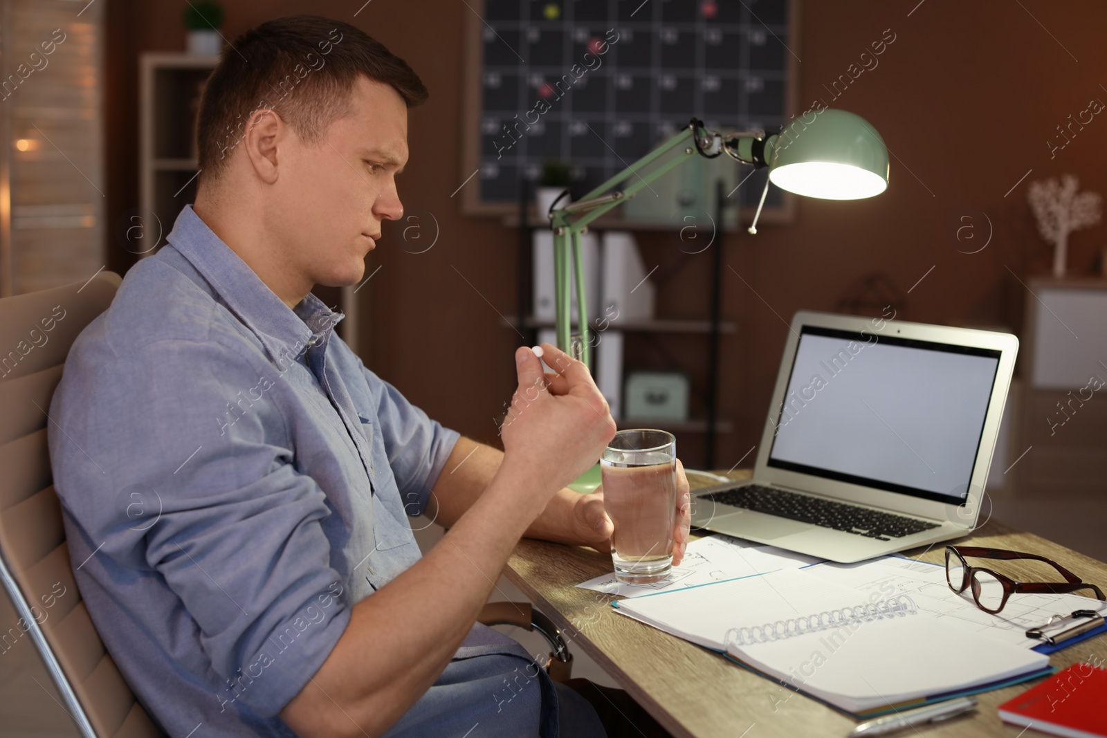 Photo of Overworked man with headache trying to take  pill in office