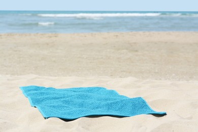 Photo of Soft blue towel on sandy beach near sea, space for text