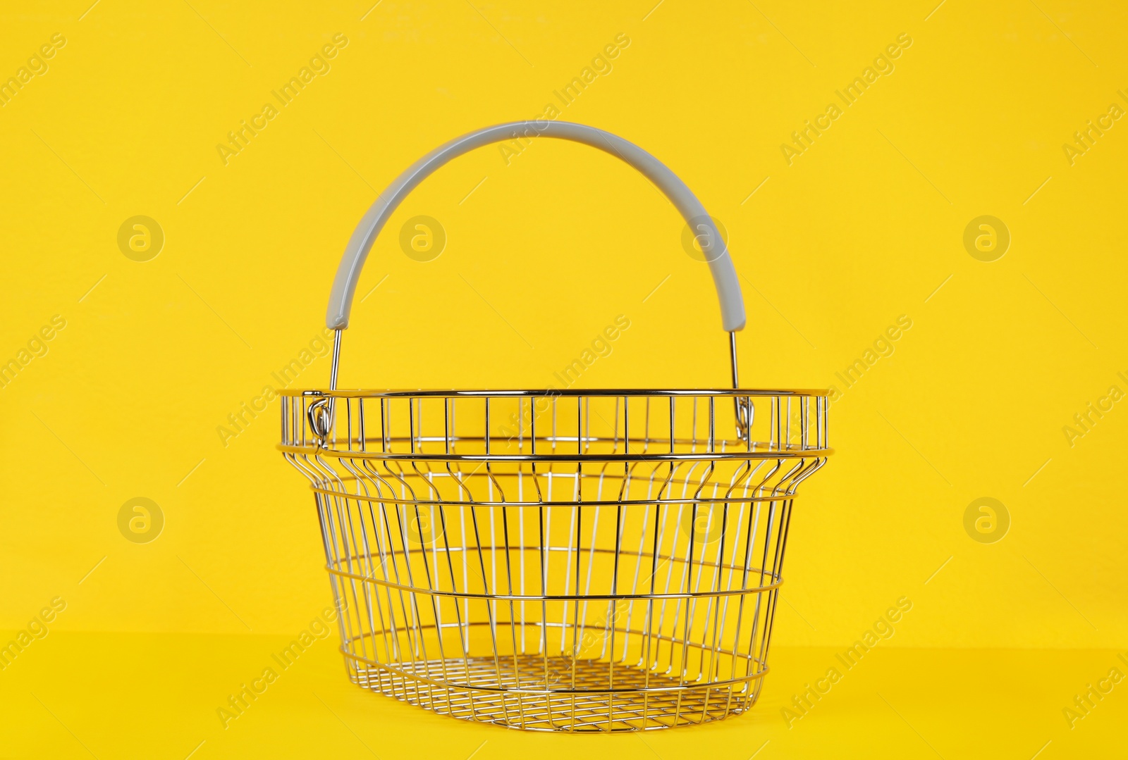 Photo of Empty metal shopping basket on yellow background