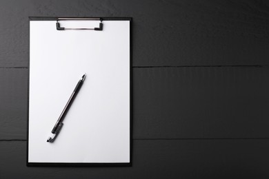 Photo of Clipboard with sheet of paper and pen on black wooden table, top view. Space for text